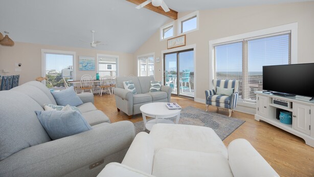 Een ruime woonkamer met een grijze bank, een witte fauteuil en een flatscreen televisie op een wit kastje.