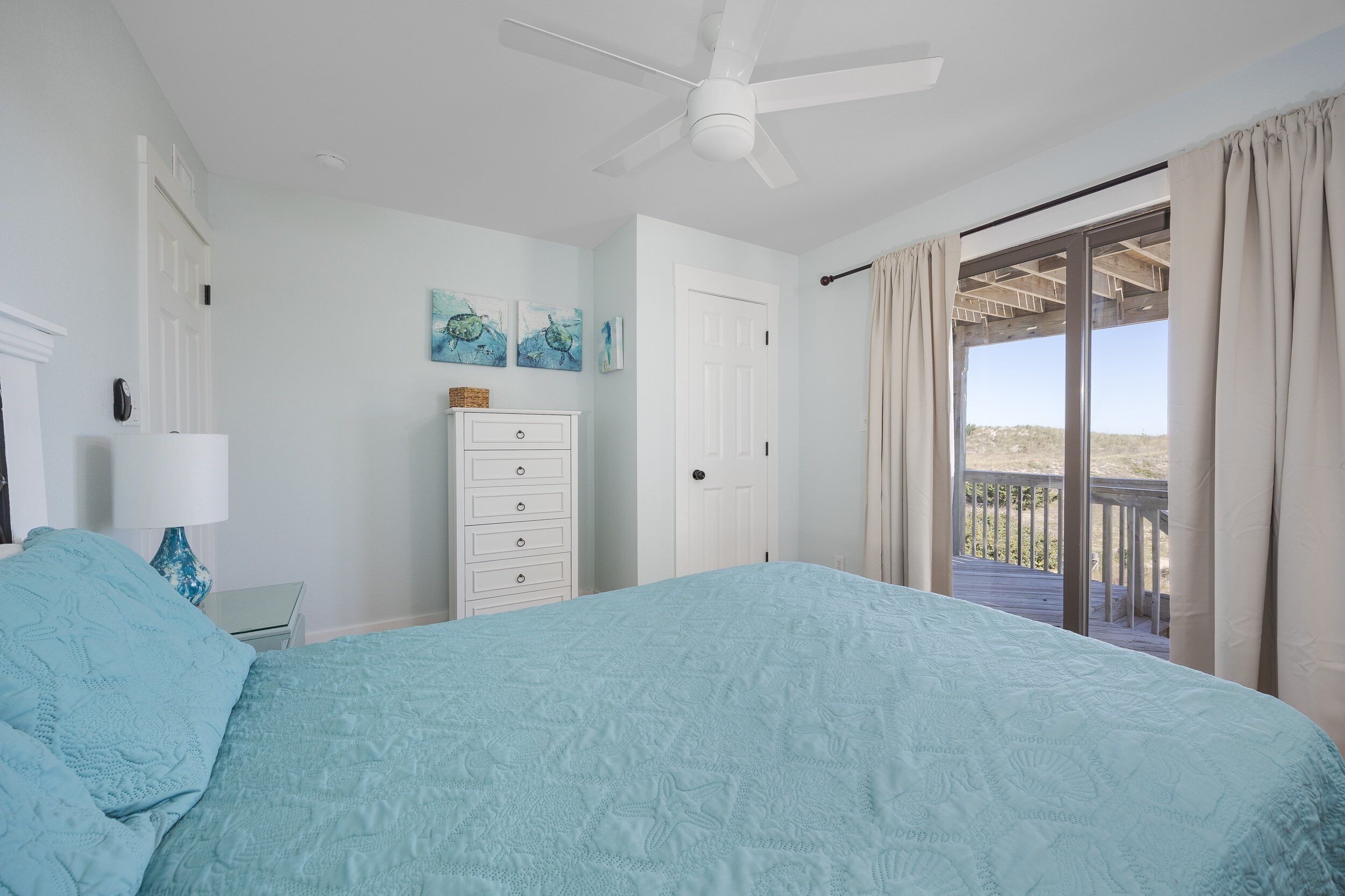 Une chambre avec un lit, une commode, un ventilateur de plafond et une vue sur un balcon.