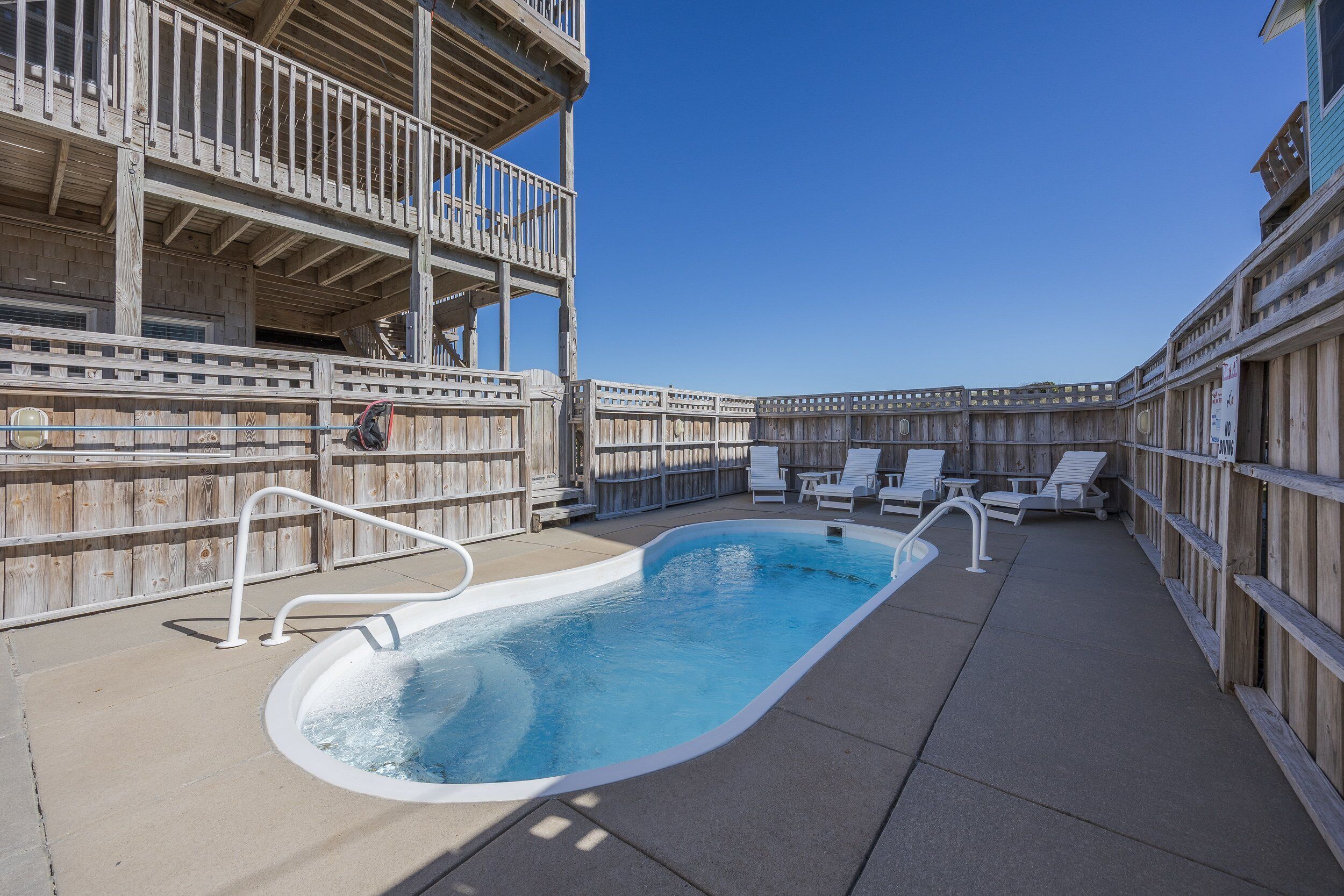 A wooden deck with a swimming pool, lounge chairs, and a wooden fence.