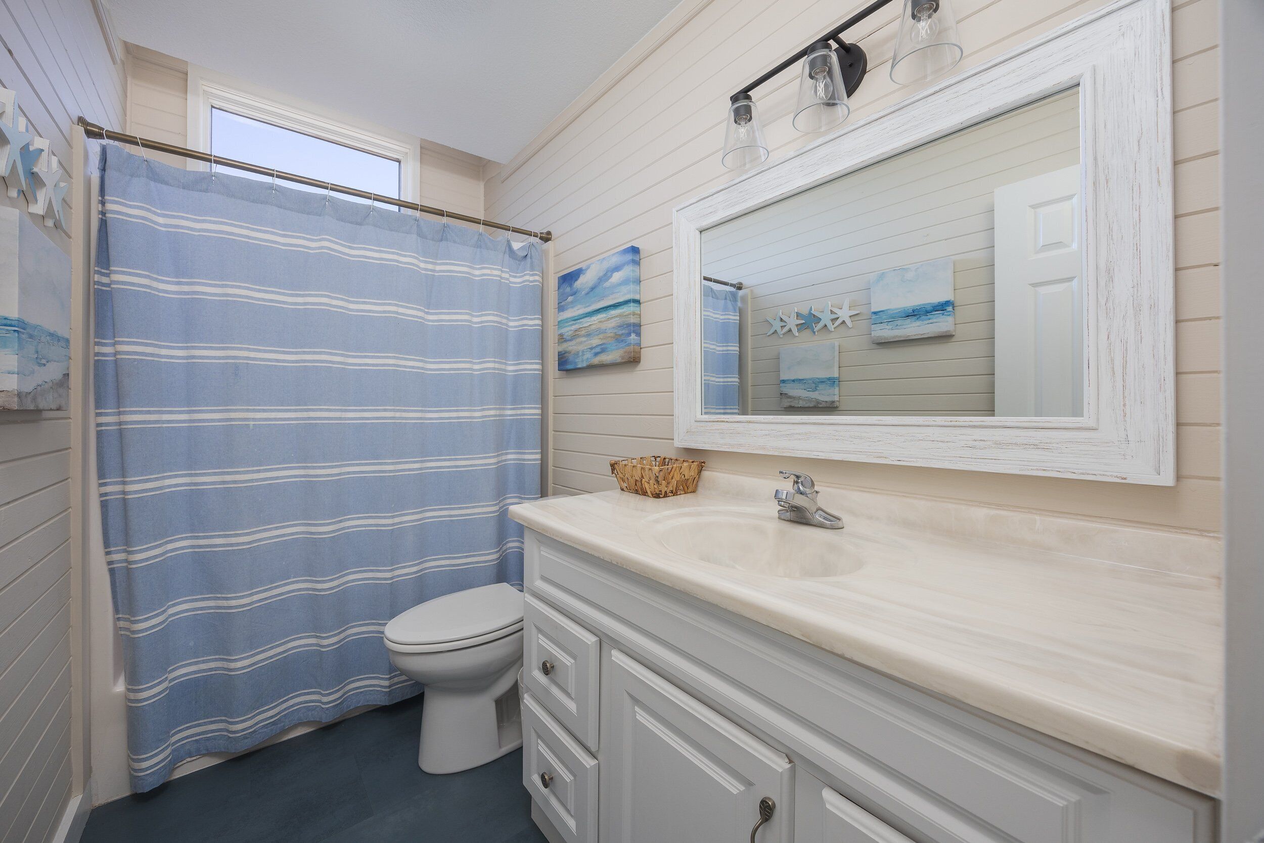 A bathroom with a striped shower curtain, a toilet, a sink with a mirror above it, and artwork on the wall.