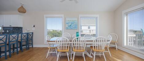 A dining area with a white table and chairs, a ceiling fan, and large windows with blinds.