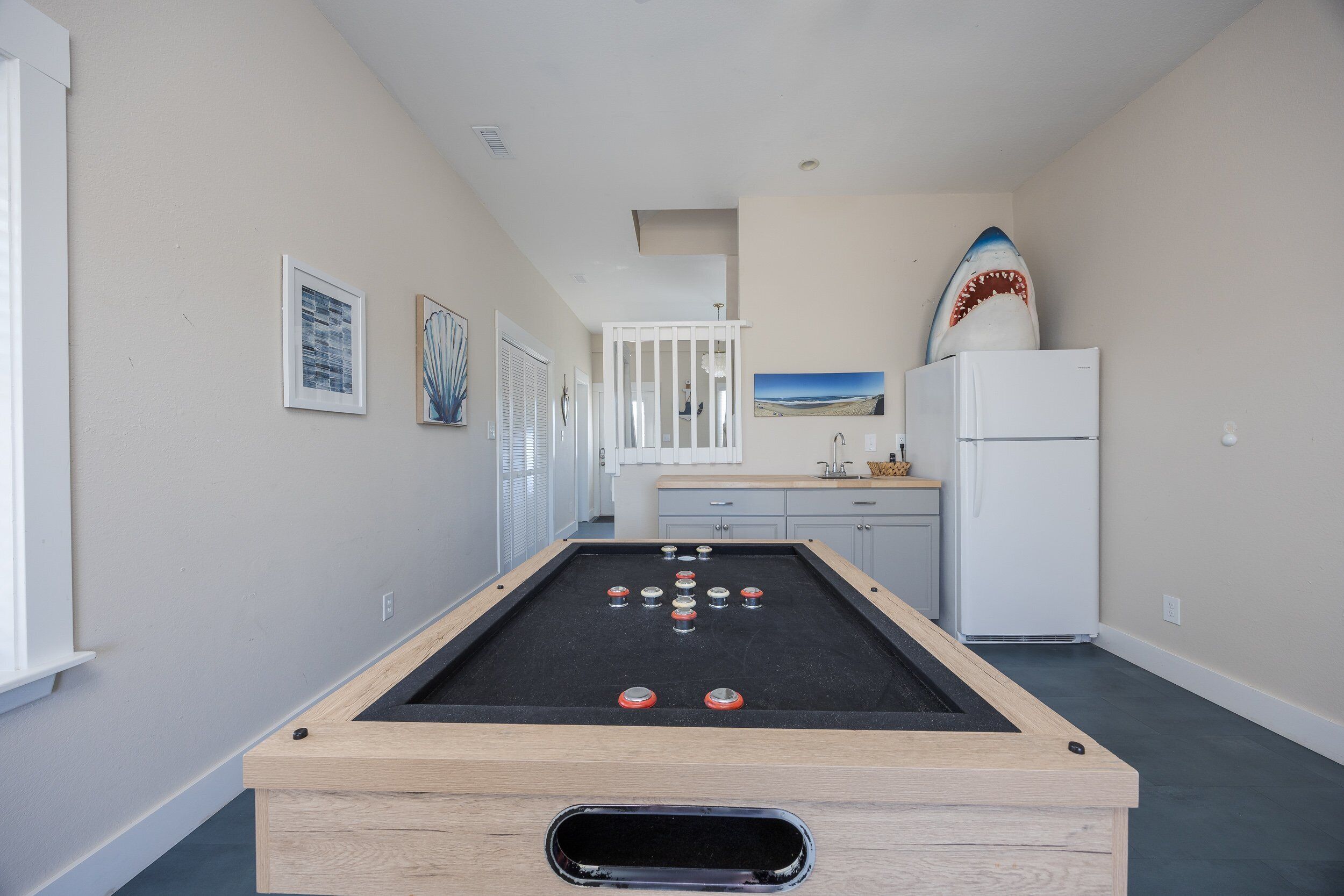 Ein Billardtisch mit Kugeln, ein Kühlschrank und ein Surfbrett in einem Raum mit Küchenzeile und Kunstwerken an den Wänden.