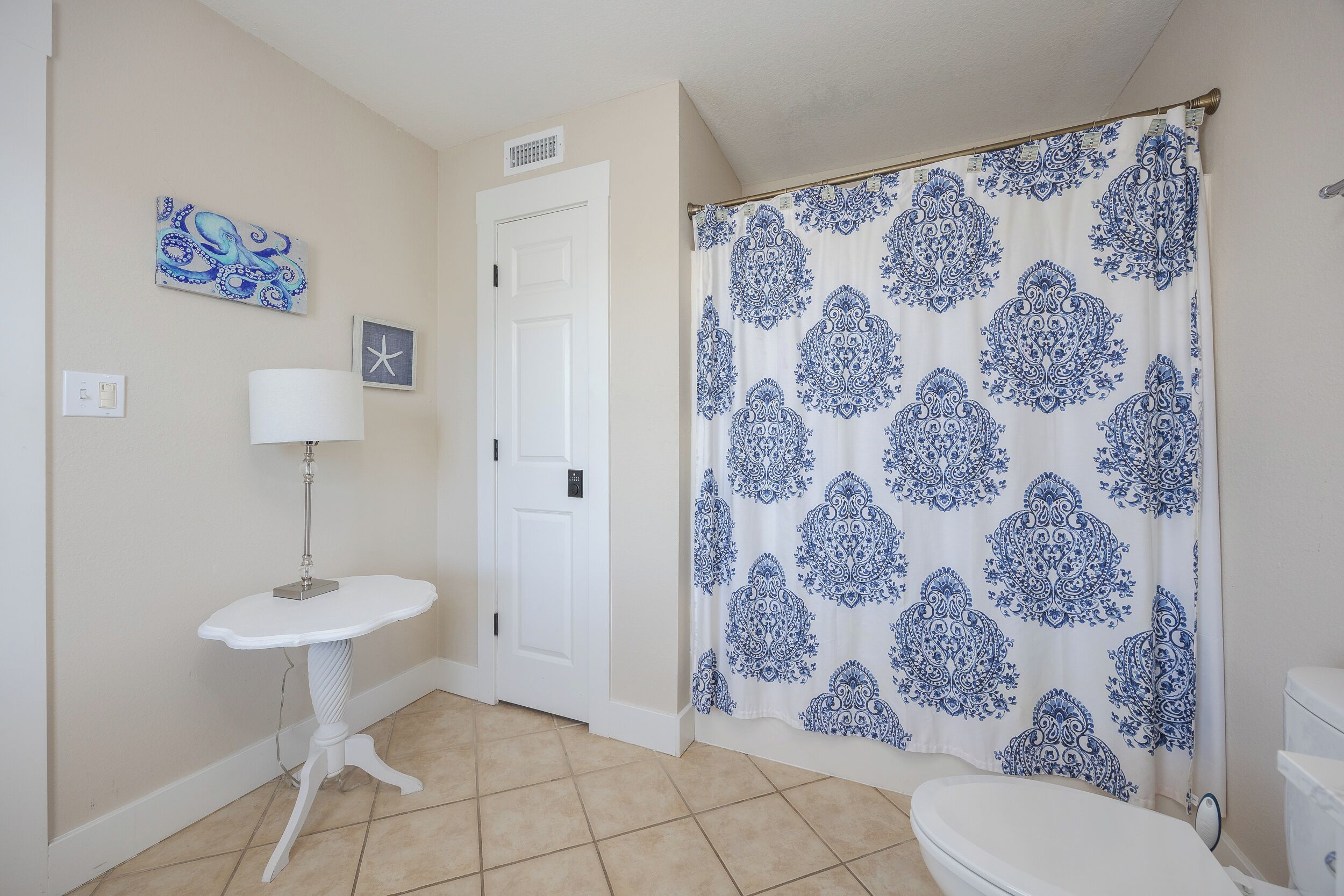 Casa de banho com sanita branca, lavatório assentado, candeeiro de parede, cortina de chuveiro com padrão paisley azul e porta com pequena decoração em estrela.