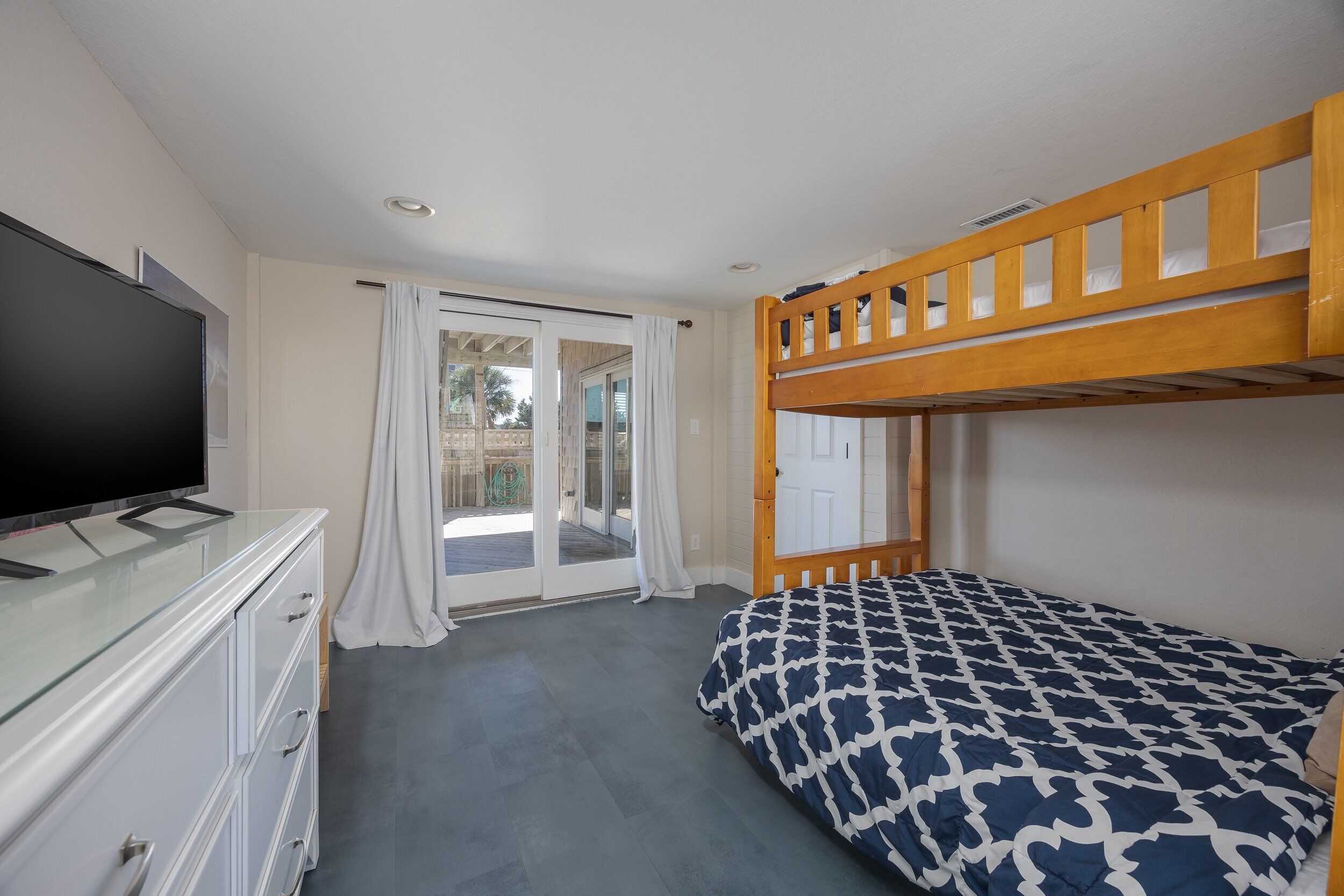 Une chambre avec un lit superposé, un téléviseur à écran plat posé sur une commode et une porte-fenêtre coulissante donnant sur un espace extérieur.