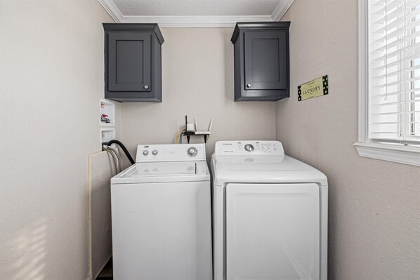 A laundry room with two white front-loading washers and dryers, dark cabinets above, and a laundry sign on the wall.