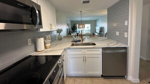 A modern kitchen with white cabinets, stainless steel appliances, and a marble countertop. - Top Floor Remodeled 2BR/2BA Beachfront Condo (New Smyrna Beach)
