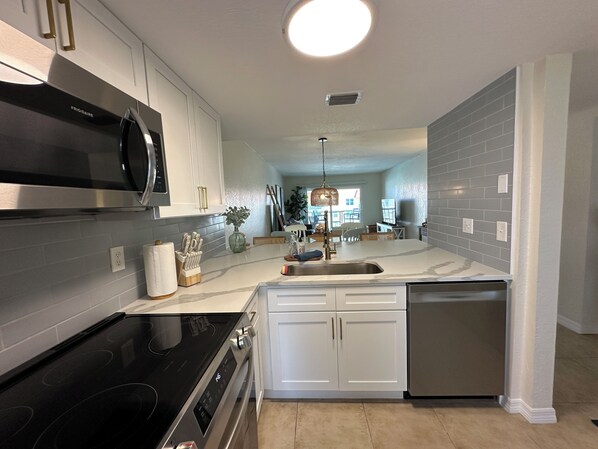 A modern kitchen with white cabinets, stainless steel appliances, and a marble countertop.