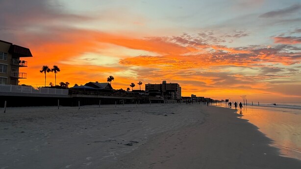 A beach with a sunset, buildings, and palm trees. - Top Floor Remodeled 2BR/2BA Beachfront Condo (New Smyrna Beach)
