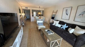 A living room with a TV, sofa, coffee table, and artwork. - Top Floor Remodeled 2BR/2BA Beachfront Condo (New Smyrna Beach)
