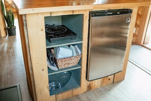 Eine kompakte Küche mit integriertem Kühlschrank, einer Mikrowelle und einem Regal mit Küchenutensilien.