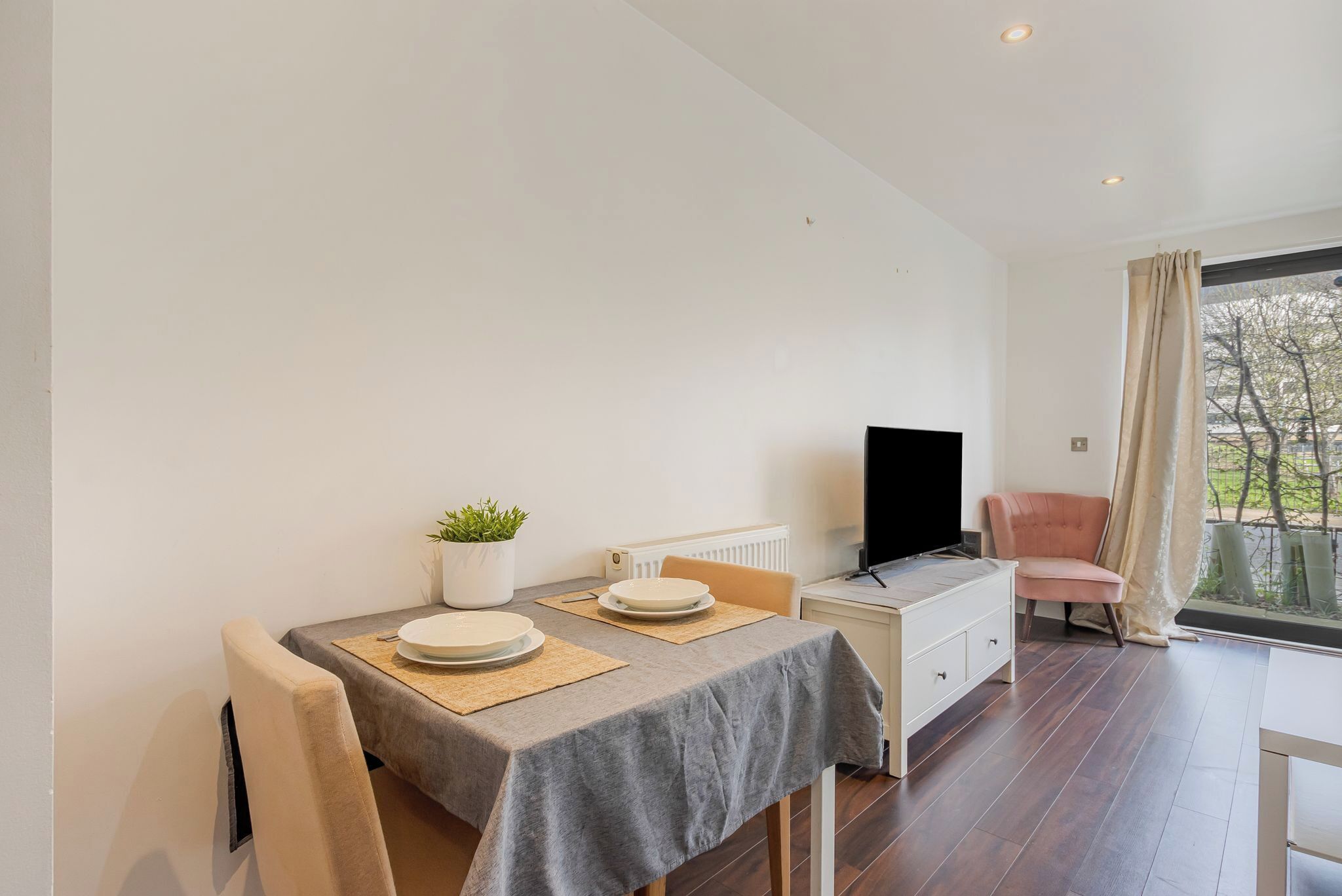 Una habitación moderna con una mesa de comedor, sillas, televisor, sofá y ventana con cortinas.