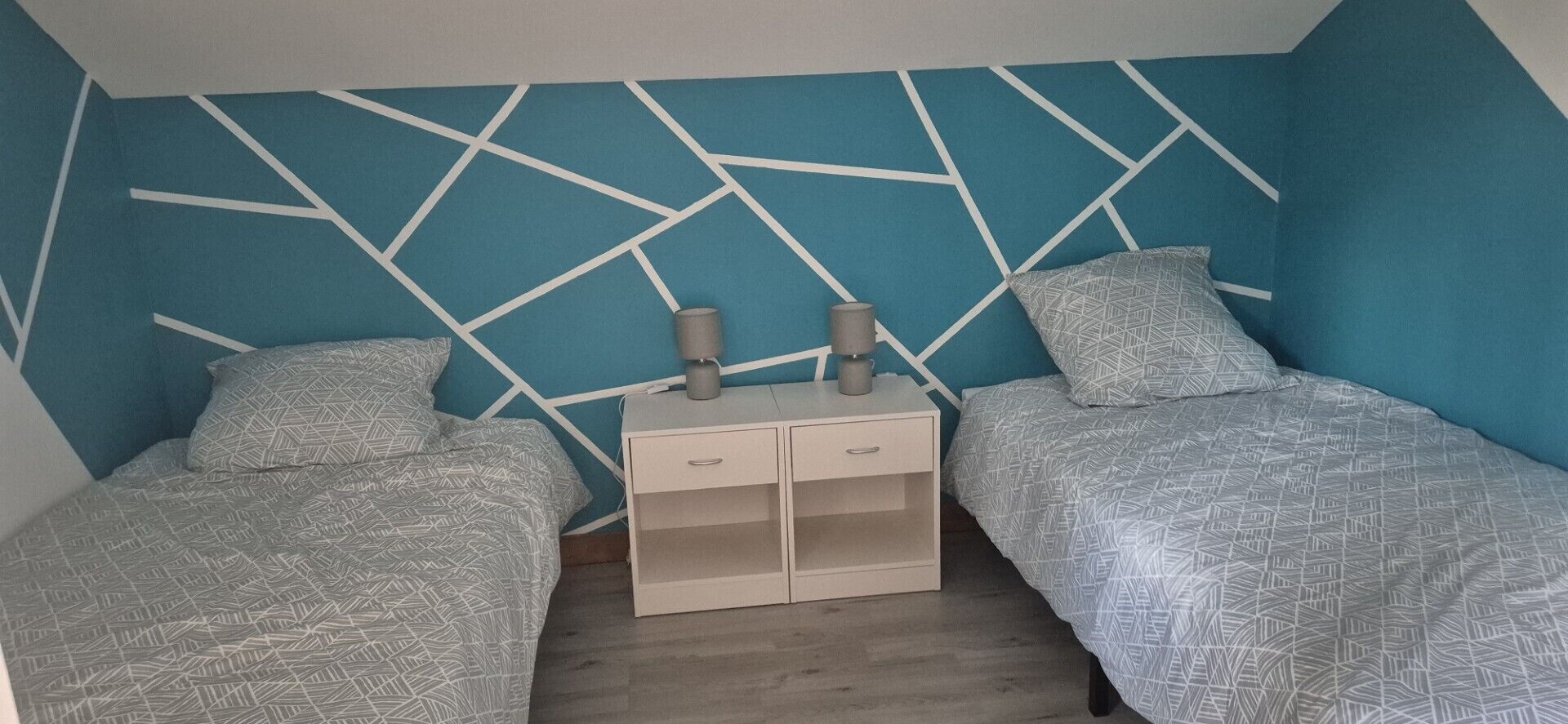 A bedroom with two beds, a nightstand, and a geometric-patterned wall.