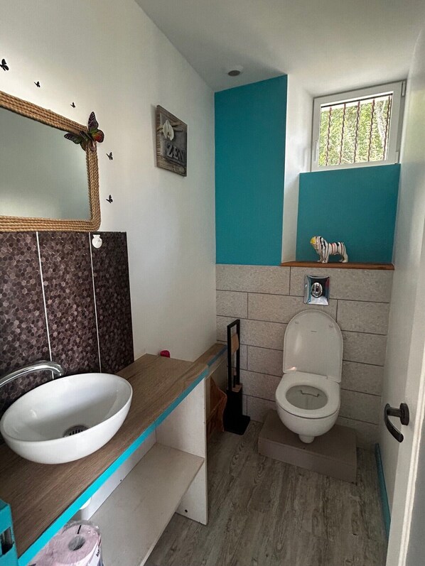 Un baño con lavamanos blanco, inodoro, espejo y ventana.