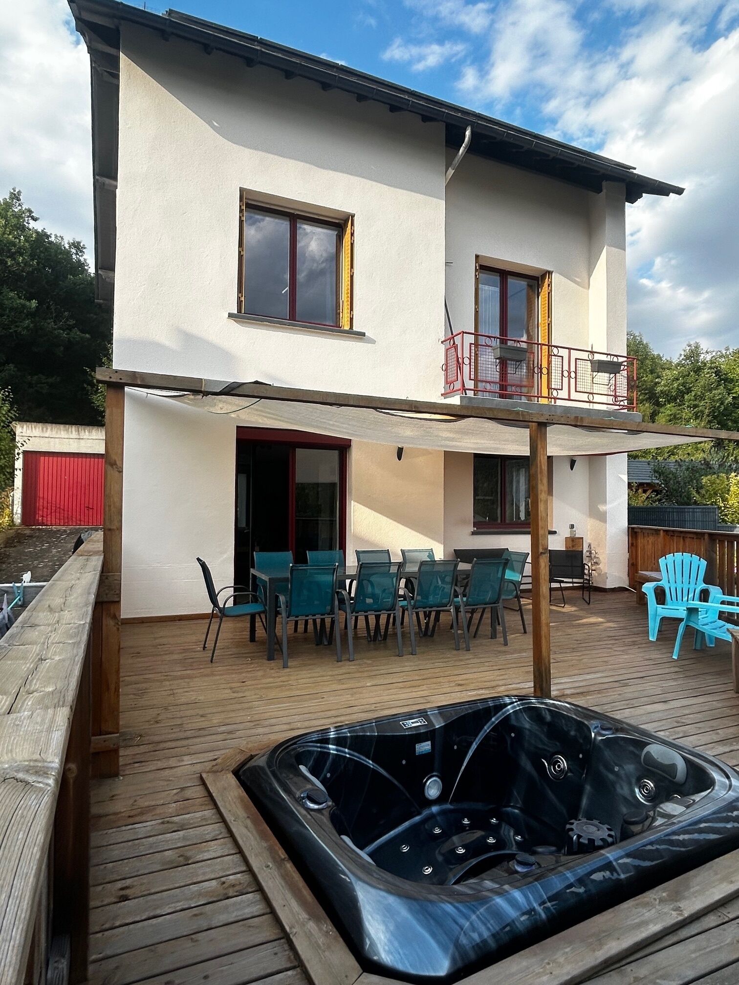 A two-story house with a wooden deck, outdoor seating, and a hot tub.