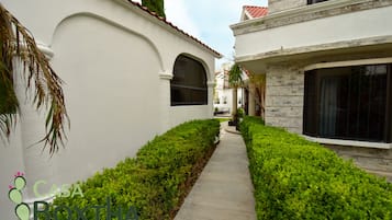 A narrow pathway flanked by well-maintained hedges and a white building with a red-tiled roof.