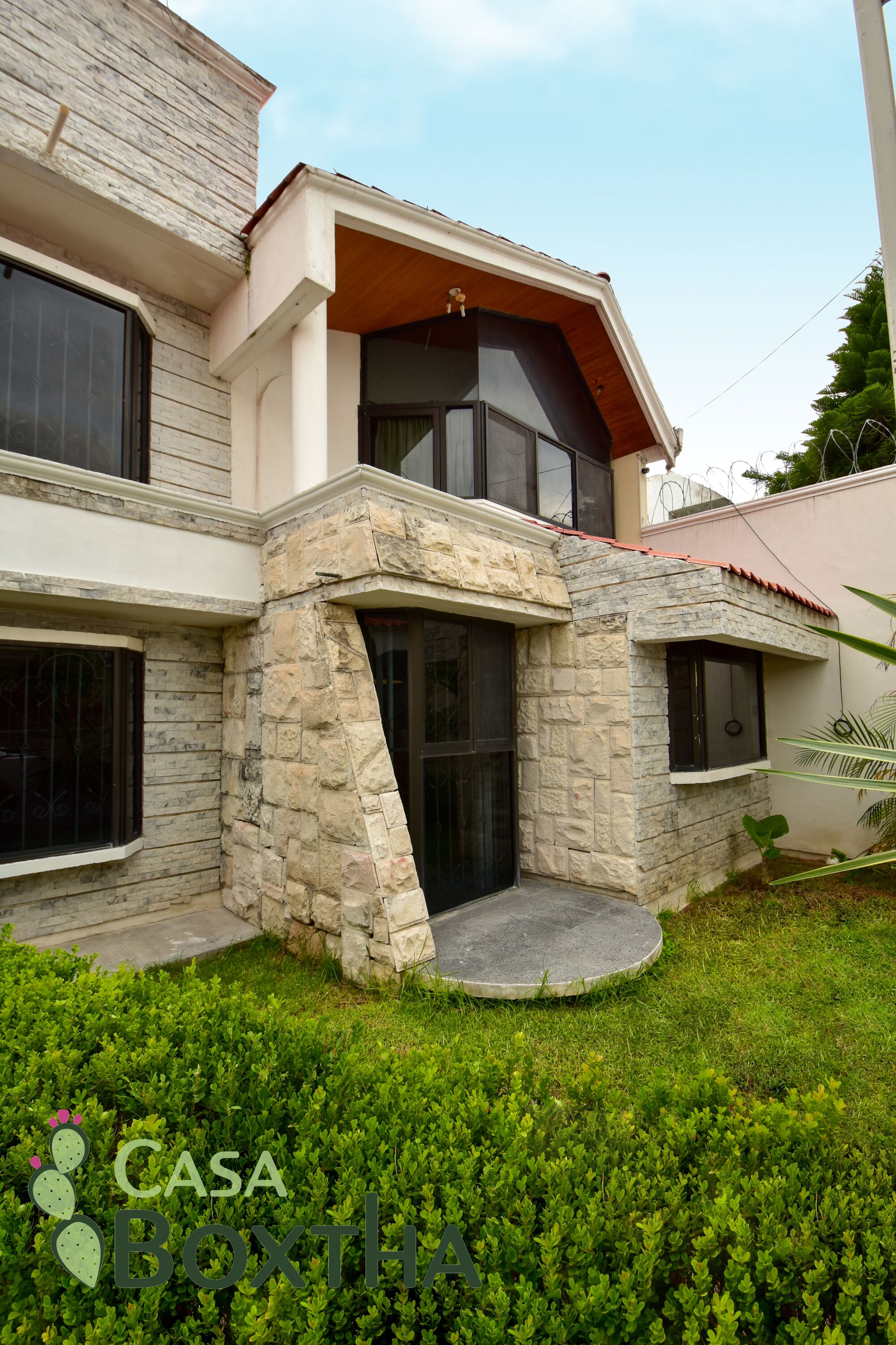 A modern two-story house with a stone facade, large windows, and a well-maintained lawn.