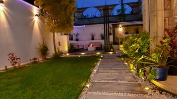 A well-lit pathway leading to a building with a garden area, potted plants, and a stone wall.