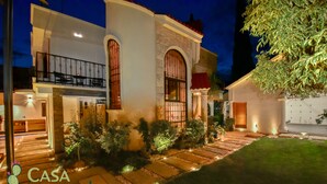 A two-story house with a well-lit entrance, a balcony, and a stone pathway leading to the door.