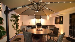 A round dining table with a fire pit in the center, surrounded by four wicker chairs.
