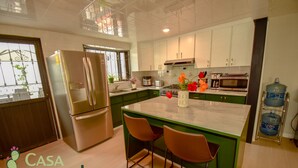A modern kitchen with a central island, stainless steel appliances, and green cabinetry.