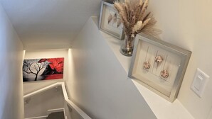 Een trap met een bekleed plateau, een lijstwerk met een afbeelding van een boom, en een vaas met gedroogde planten.