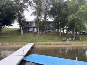 Una proprietà sul lago con un molo, una casa con un balcone e una zona verde con sedie.