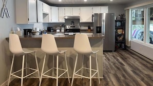 A modern kitchen with white cabinets, a stainless steel refrigerator, and a bar area with white stools. - Lake Seven, Frazee, MN (Frazee)