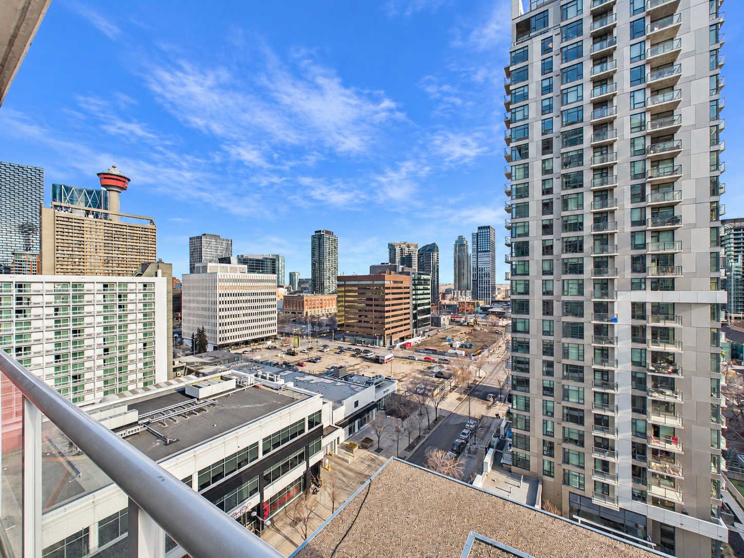 A high-rise building with multiple floors and balconies, surrounded by other buildings and a clear sky.