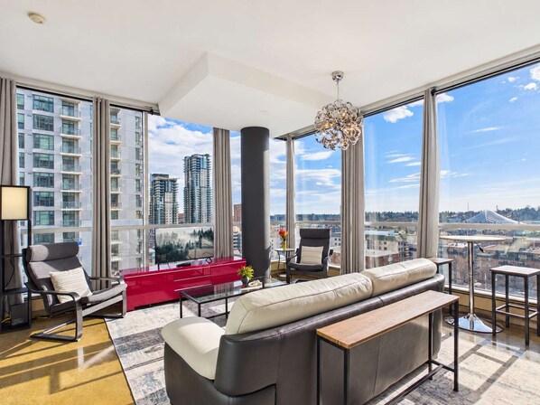 A modern living room with a large window, a red sofa, a black armchair, and a view of high-rise buildings.