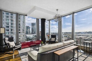 A modern living room with a large window, a black sofa, a red accent wall, and a view of a cityscape.