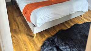 A bedroom with a bed, two nightstands, a wooden floor, and a black furry rug.