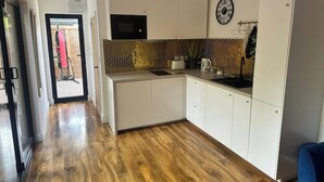 A compact kitchen with white cabinets, a microwave, and a clock on the wall.