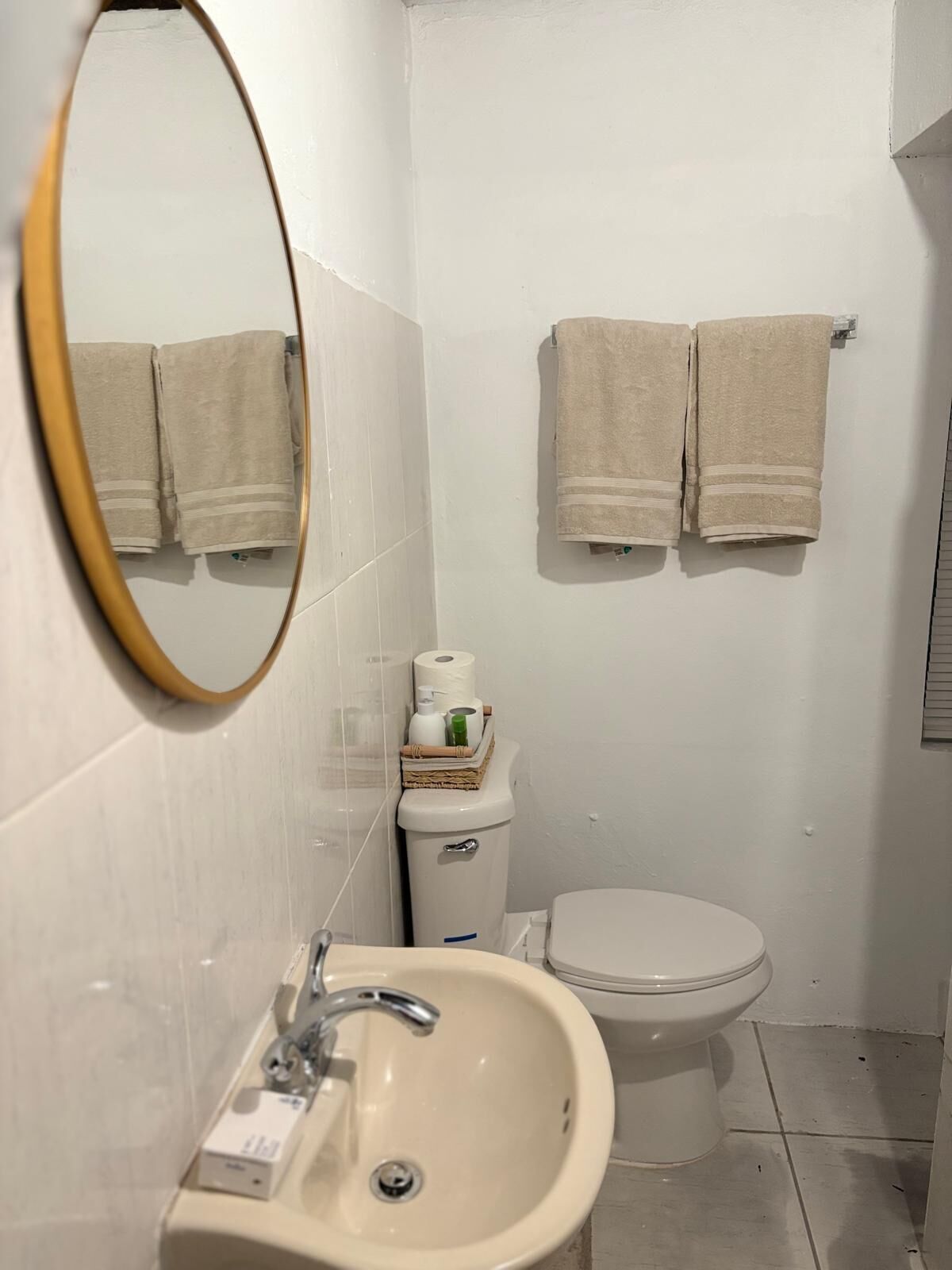 Een kleine, schone badkamer met een wastafel, toilet en twee handdoeken aan de muur.