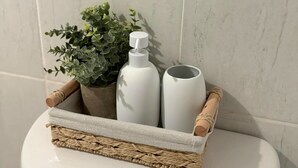 Un bagno con un water, un cesto di vimini contenente una pianta in vaso e due bottiglie bianche.