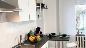 Una cocina moderna con un lavamanos de acero inoxidable, horno empotrado, armarios blancos y un comedor con una silla blanca.