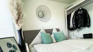 Un dormitorio con cama, un reloj en la pared, un cuadro enmarco, un perchero y un jarrón con plantas secas.