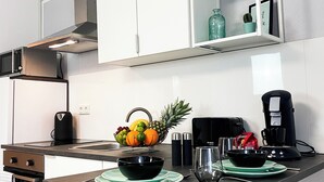 Una cocina moderna con armarios blancos, una campana extractora de acero inoxidable, una cafetera y un frutero sobre la encimera.