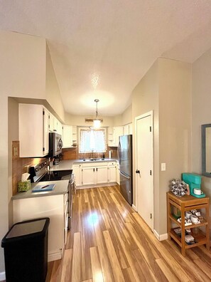 A kitchen with wooden flooring, white cabinets, a stainless steel refrigerator, and a coffee maker on a wooden side table.