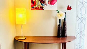 Ein Zimmer mit einem Holztisch, einer Lampe und einem Blumenbild.