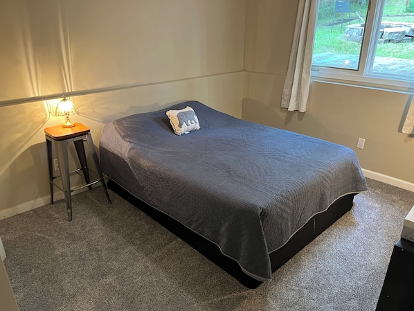 A bedroom with a bed, a nightstand with a lamp, and a window with curtains.