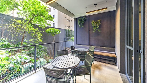 Un área de estar moderna al aire libre con una mesa redonda y sillas, un banco y vistas a un paisaje urbano y vegetación.