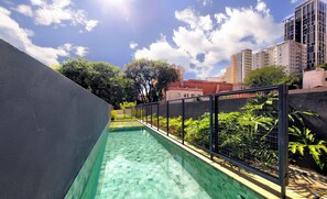 A swimming pool with a tiled floor, surrounded by a black metal fence, and a view of buildings and trees in the background. - Studio With Balcony 100m From Puc-pompeia Puq0208 (São Paulo)