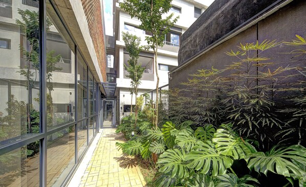 A narrow corridor with glass walls, a tiled floor, and lush tropical plants. - Studio With Balcony 100m From Puc-pompeia Puq0208 (São Paulo)