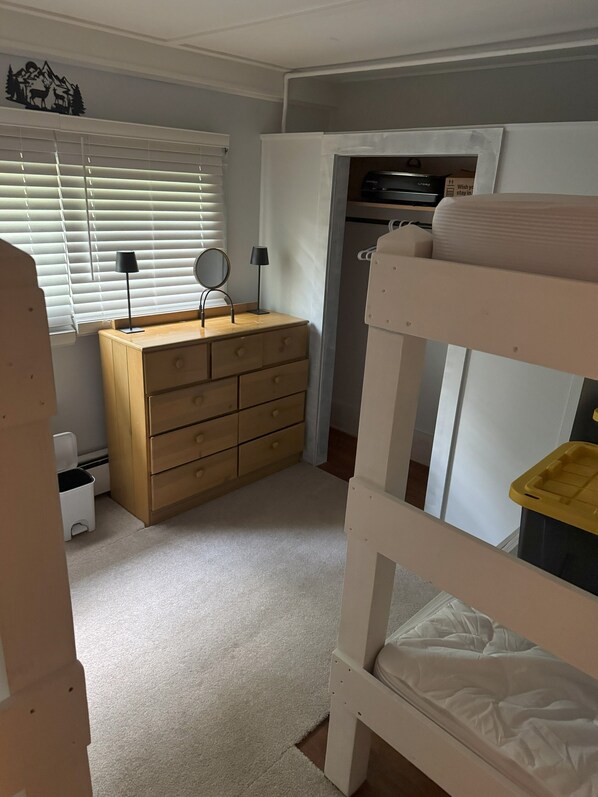 A child's bedroom with a bunk bed, a dresser, a mirror, and a window with blinds.