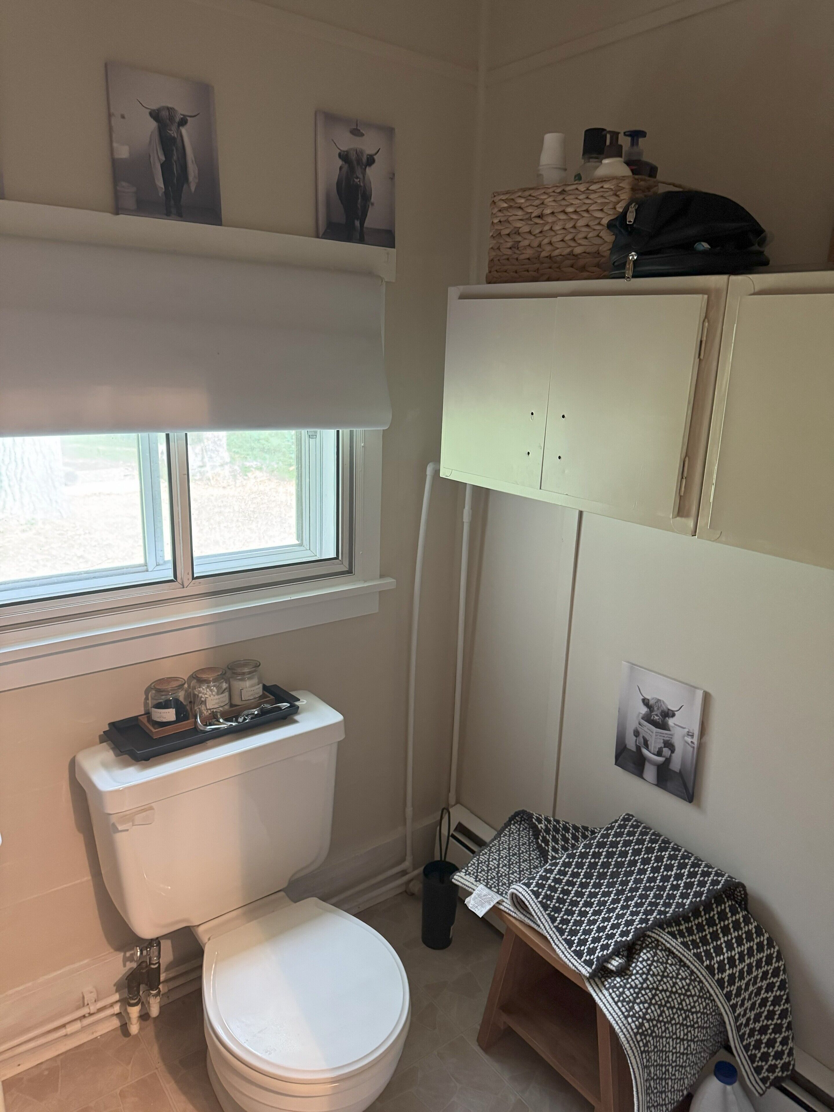 A compact bathroom with a toilet, a window, and a shelf with toiletries.