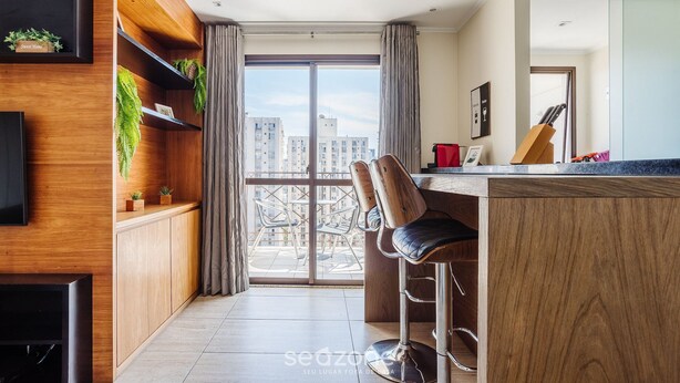 A modern kitchen with wooden cabinetry, a bar area with stools, and a large window offering a city view. - Elegant Apt, Near Ibirapuera - Qsa1405 (São Paulo)