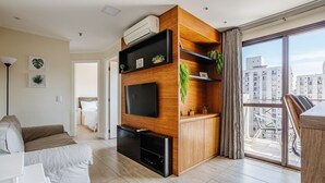 A modern living room with a flat-screen TV, wooden shelving, and a balcony with a city view. - Elegant Apt, Near Ibirapuera - Qsa1405 (São Paulo)