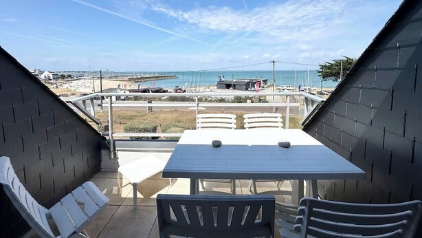 A terrace with a table and chairs, overlooking a beach and marina. - Duplex plein charme – Face mer & déco moderne (Quiberon)