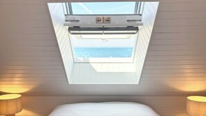 A room with a skylight above a bed, two bedside lamps, and a view of the sea. - Duplex plein charme – Face mer & déco moderne (Quiberon)