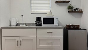 Una cucina compatta con lavandino, macchina del caffè, microonde e frigorifero.